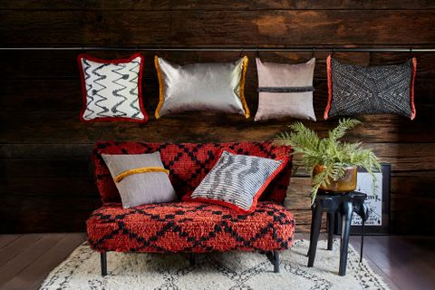 a series of rectangular and square shaped cushions in a different colours and styles from the abigail ahern collection are on a wall and some on a red and black styled sofa 