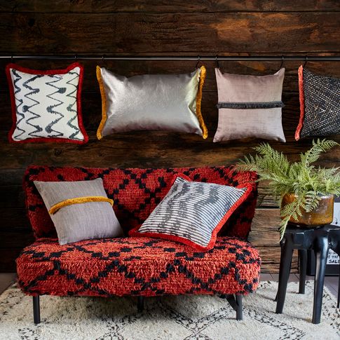 a series of rectangular and square shaped cushions in a different colours and styles from the abigail ahern collection are on a wall and some on a red and black styled sofa 