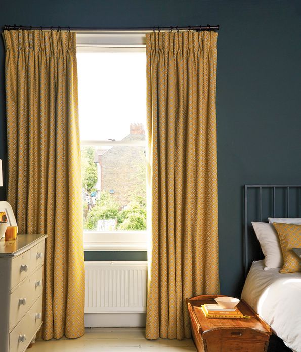 Yellow curtains fitted to a rectangular shaped window in a bedroom decorated in yellow and dark blue