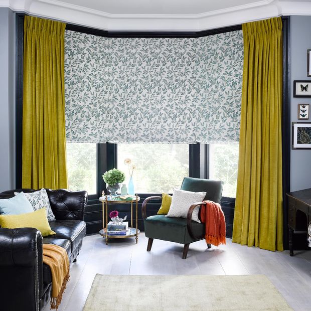 lyon sulphur curtains and delizia teal roman blinds in bay window of living room with black leather sofa and dark armchair