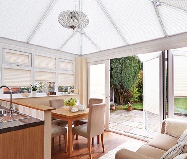 Conservatory dining room with bi-fold doors and montoya sand pleated roof blinds
