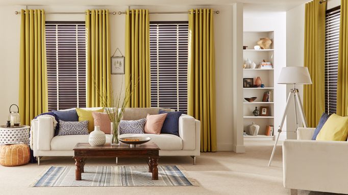 Modern living room with large windows dressed with curtains and faux wooden blinds in dark brown 