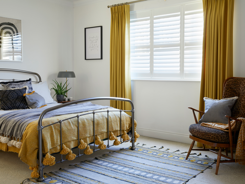 Bedroom with curtains in bright yellow fabric and white shutters in the windows 