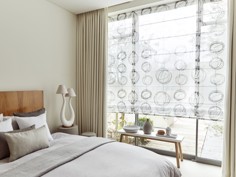 A bedroom with a large window fitted with a Voile Roman blind in Swirl Dusk