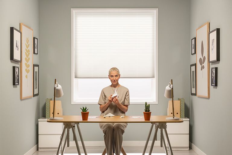 Woman sitting in front of pure white pleated blind from Hillarys advert