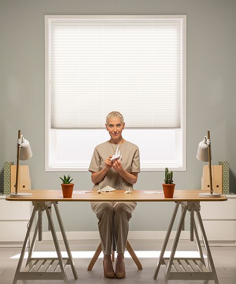 Woman sitting in front of pure white pleated blind from Hillarys advert