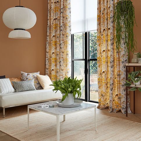 Florally decorated curtains and matching white blinds are fitted to a door window in a living room with orange and white colours