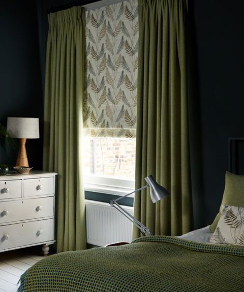 Green plain curtains over leaf motif Roman blind in bedroom