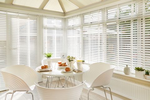Bright dining area in a conservatory with White Faux Wood conservatory blinds and pleated conservatory roof blinds