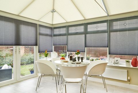 Relaxing dining area in a conservatory fitted with Sand Pleated roof blinds and grey Pleated side blinds