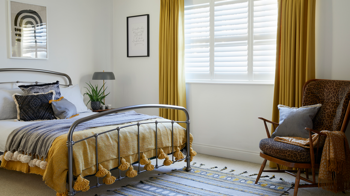 Bedroom with ochre curtains over white shutters