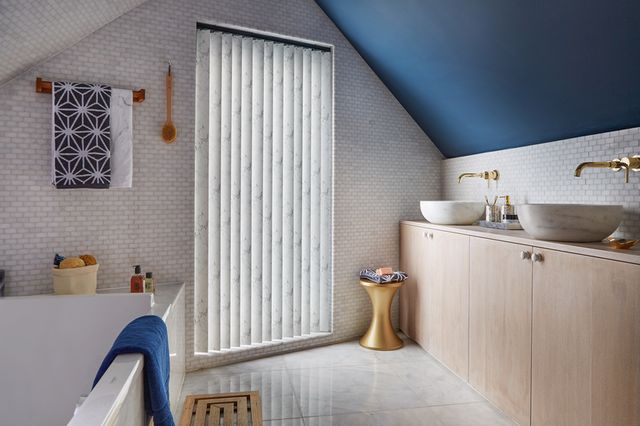 Alessio Dark vertical blinds fitted to a window in a bathroom with stone floors, tiled walls and a bath tub