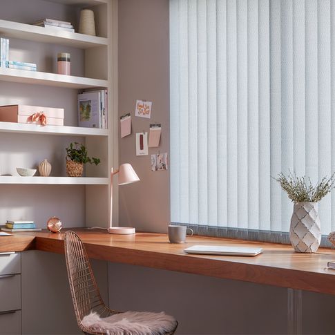 Modern home office with build in desk and shelves and windows dressed with pale blue vertical blinds
