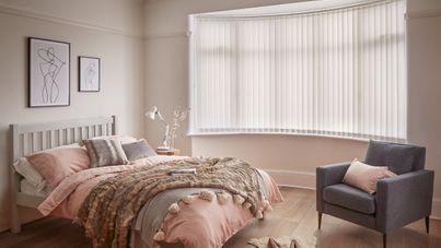 Minimal luxe bedroom with soft furnishings and a bow window dressed with light cream vertical blinds 