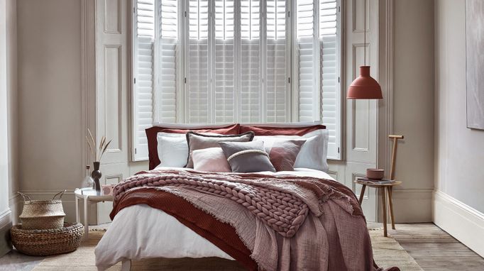 Tall tier-on-tier shutters covering a luxurious bedroom window. The shutters are white, with the louvres closed in the bottom half