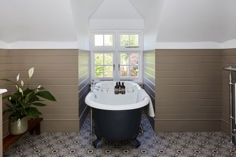 Two latch operated windows fitted on a window sill in a bathroom decorated with white and brown coloured walls while the bath tub sits in the middle