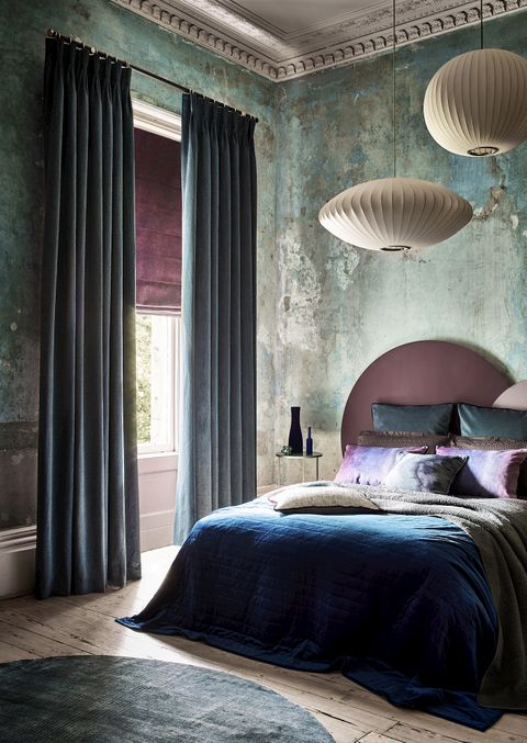 A faded glamour bedroom featuring blue curtains over a purple Roman blind at a single window 