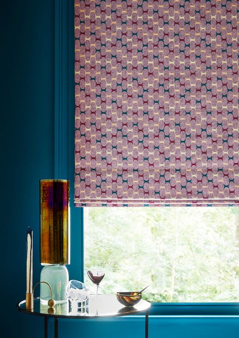 Close up detail of window with pink geometric Roman blind and dark teal painted walls