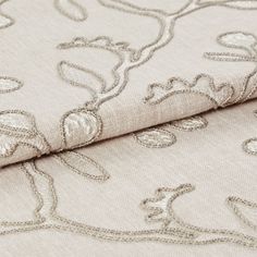 Folded fabric in a neutral colour with a repeating leaf and stem pattern in a slightly darker style