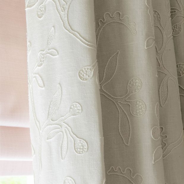 close up cream curtains featuring delicate embroidery hanging on bedroom window 