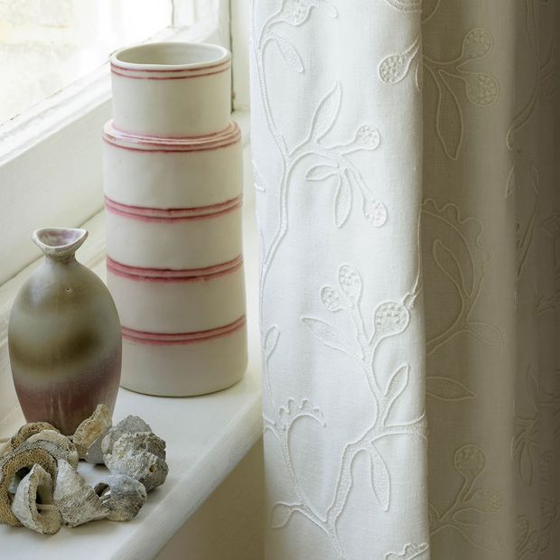 Close up of bedroom window dressed with cream curtains featuring delicate embroidery