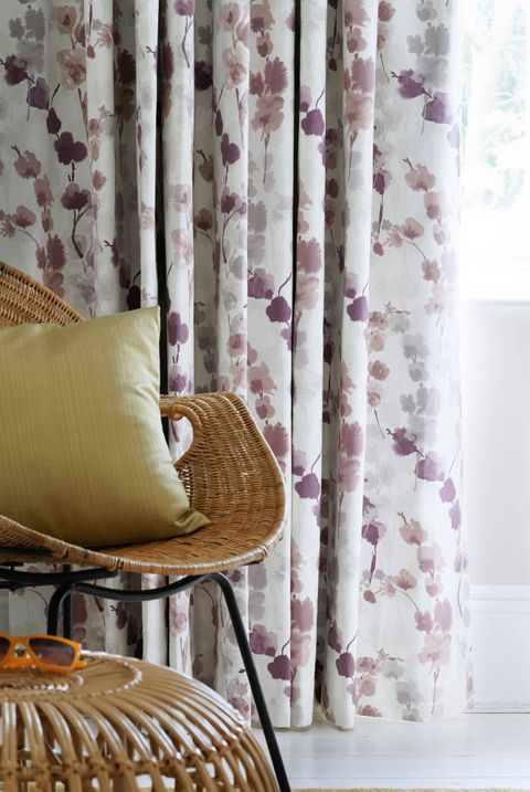 Close up detail of purple floral curtains and wicker chair 