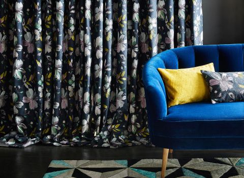 Close up detail of blue sofa with dark floral curtain behind
