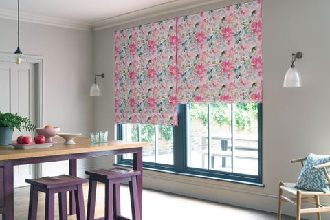 Pink, blue and purple floral roman blinds in a white dining room covering a blue window 