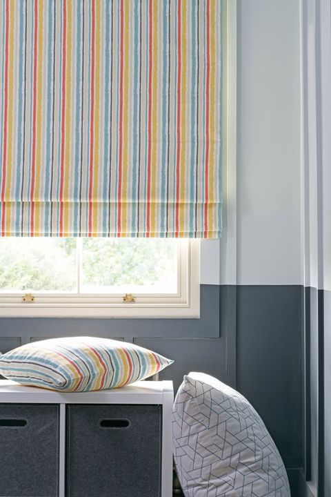 Striped roman blinds with mustard, orange and light blue colors and matching cushion in an attic bedroom