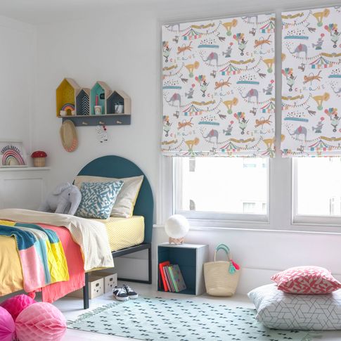 A children's bedroom featuring two windows that have a white blinds dotted with multi coloured circus animals