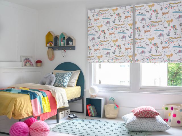 A children's bedroom featuring two windows that have a white blinds dotted with multi coloured circus animals