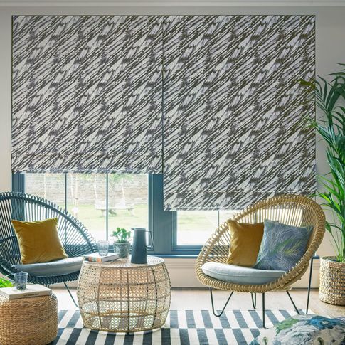 Black and white wave patterned roman blinds in a garden room decorated with wicker furniture and wicker chairs are placed with plain mustard and blue cushions.
