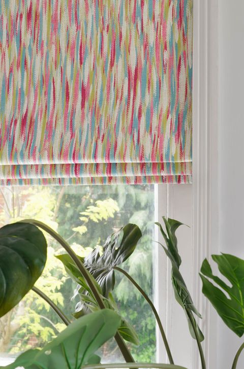 View of a corner of window covered with multi colored patterned roman blinds. 
