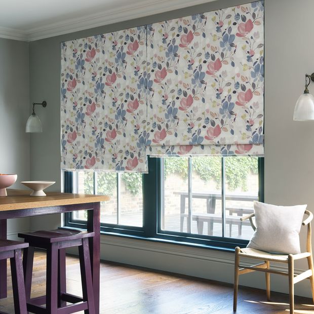 Layers of a Roman blind featuring a lavender, rose and yellow coloured floral pattern hang neatly in front of a window.