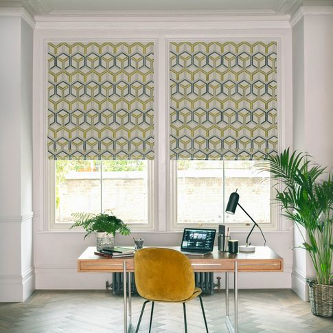 Window of home office behind office table dressed with roman blinds printed with geometric shapes in mustard and grey colors on white background
