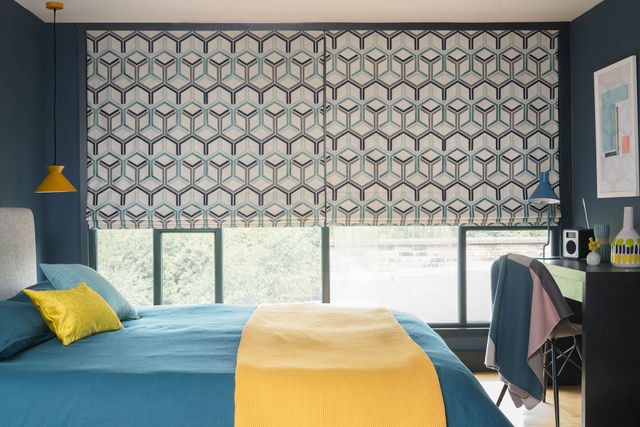 A geometric blue, white and black circular design featured on a Roman blind which is behind a blue bed with a yellow throw