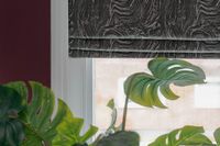 A green monstera deliciosa plant rests below a white window on a deep red wall