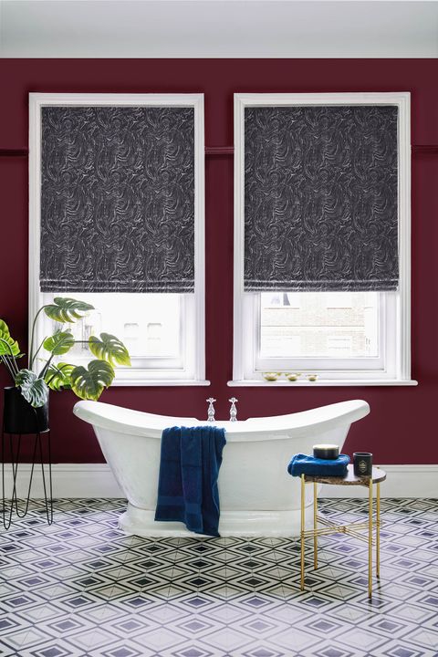 A deep wine red bathroom featuring two white windows. The windows have a deep grey marble inspired Roman blind on them. 