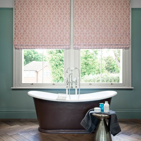 Two big windows in bath dressed with pink roman blinds featuring geometric shapes.