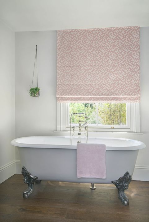 Layered geometric peach and cream coloured Roman blinds featured neatly on a window in white bathroom 