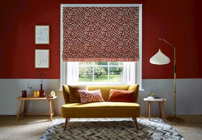 A red and white room with a bright yellow couch that sits under the window. The window is covered with a Roman blind that features a red and white linear design