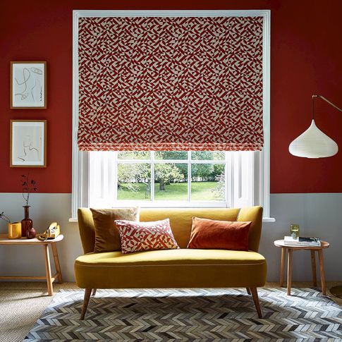 A red and white room with a bright yellow couch that sits under the window. The window is covered with a Roman blind that features a red and white linear design