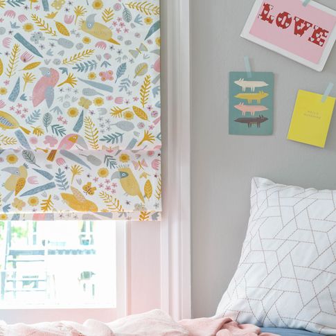 Corner view of kids bedroom window dressed with roman blinds featuring tucan print on white background