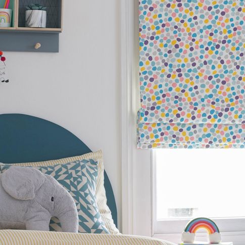 Corner view of a kids white bedroom window dressed with roman blinds featuring multi-coloured dot pattern on a white background