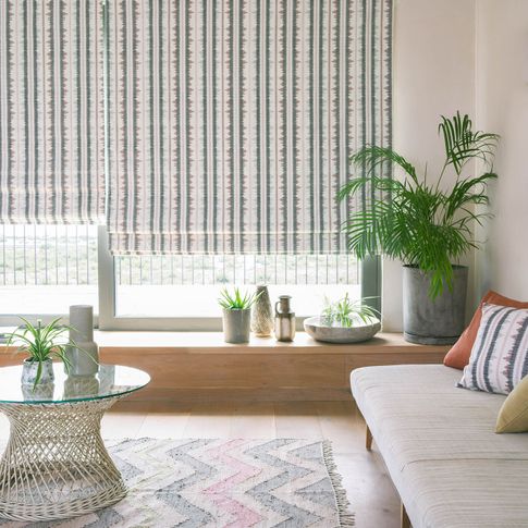 A stripy white, brown and green Roman blind hangs over a window in a white room
