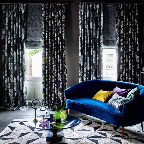 Windows in grey Living room dressed with multi-coloured floral embroidery on a navy background  curtains,  floral print in dark grey shades and silver  curtains and  textured shimmering grey roman blinds.