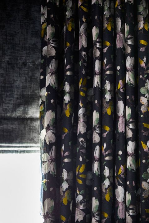 A close up of a charcoal Roman blind under a floral print curtain