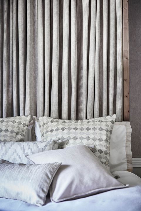View of bed with grey striped curtain headboard covered with plain, printed and patterned cushions