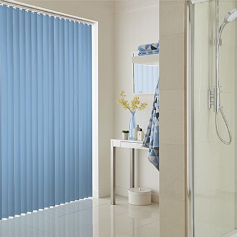 Blue coloured vertical blinds fitted to a tall and wide window in a bathroom that is decorated in white