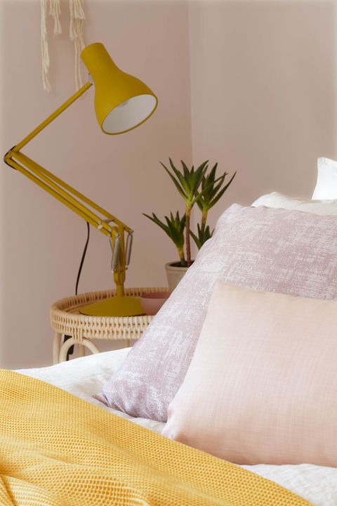 View of bed covered with mustard shrug and cushions of cream and light pink color by mustard lamp